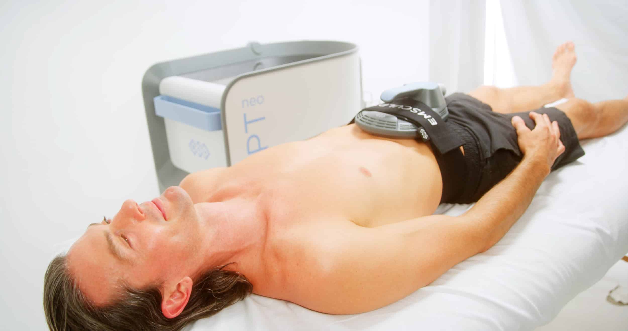 man laying down with emsculpt neo non-surgical body contouring device on bare stomach