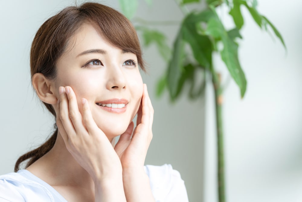 Smiling young woman touching the smooth, shining skin of face after receiving a chemical peel.