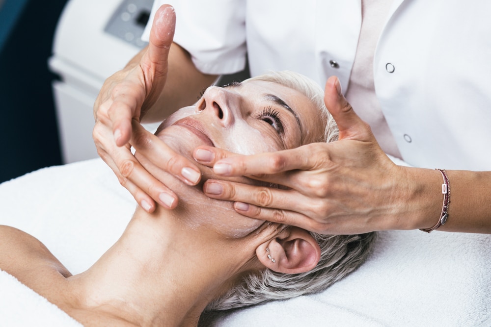 Older woman happily having a chemical peel applied to her face for more youthful, brighter skin.