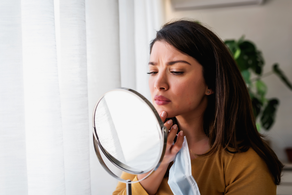 Woman looking in mirror at new pimple on face