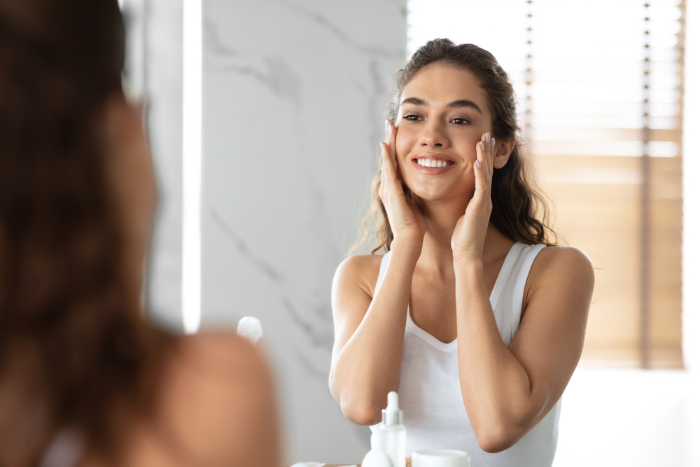 Beautiful woman smiling at herself in the mirror with glowing skin after cosmetic treatments.