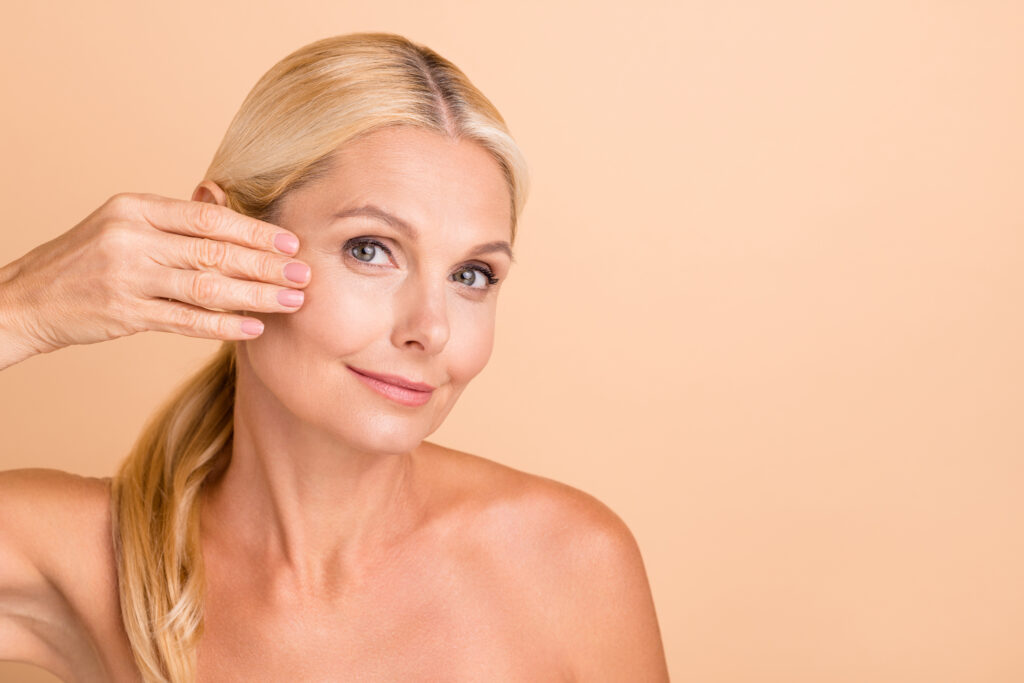 Mature woman touching her cheek and smiling, showing smooth skin and subtle lift after liquid facelift