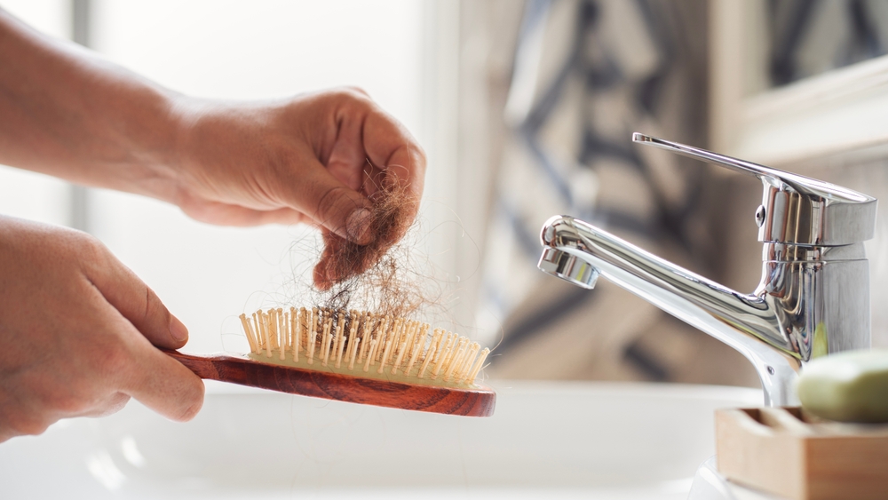 Woman holding a hairbrush with noticeable hair shedding.